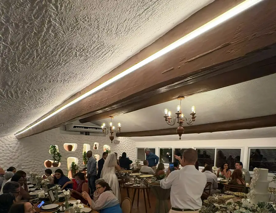 O Mezanino durante um casamento: vigas de madeira, luz quente no teto, lustres de ferro e a mesa comprida posta